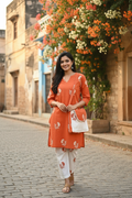Model wearing orange rust floral block print coord set with matching sling bag on floral street background